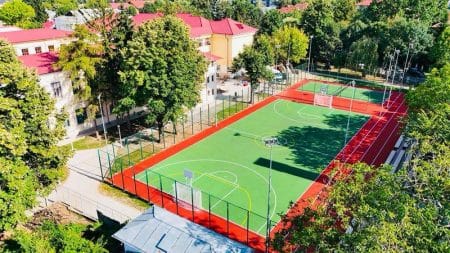 Teren de sport în curtea unei școli din Bacău, înconjurat de copaci și clădiri colorate.