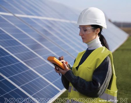 Ingineră verificând panouri solare cu dispozitiv de măsurare.