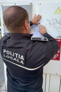 Polițist local verificând anunțuri pe un panou publicitar în Bacău.