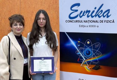 Tânără elevă primind diplomă la evenimentul Evrika cu afiş în fundal.