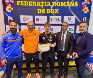 Boxer tânăr pe podium cu trofeu la competiție națională în fața bannerelor Federației Române de Box.