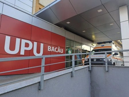 Ambulanță la intrarea în UPU Bacău lângă fațada roșie.