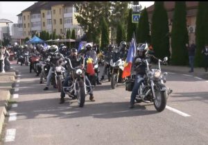 O colecție de motociclete cu Riders purtând drapele, participanți la un eveniment în stradă.