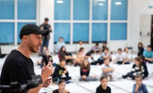 Vorbitator ținând microfonul într-o sală plină de copii și participanți.