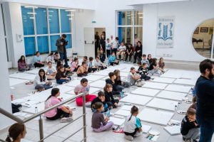 Grup de copii desenând pe pereți albi într-o bibliotecă din Onești, la o activitate artistică colect.