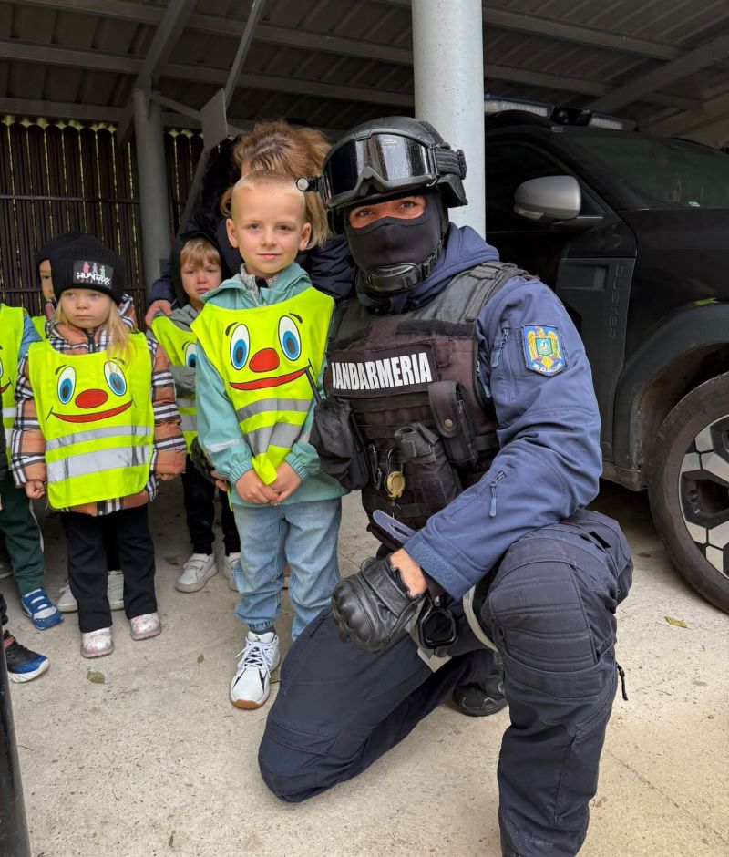 Cop jandarm în echipament de protecție alături de copii în vizită la unitatea de poliție.