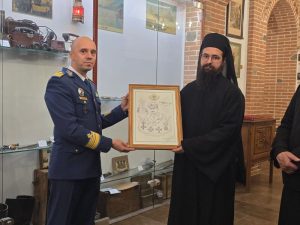 Ofițer militar înfățișând un cadru cu un document în fața unui călugăr într-un muzeu.