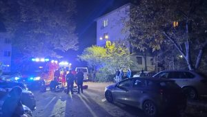 Echipajul de ambulanță și echipaje de prim ajutor acționează lângă mașini parcate în fața blocurilor.